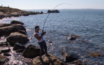 A person fishing from a rocky coastal shoreline, casting a line into the ocean.