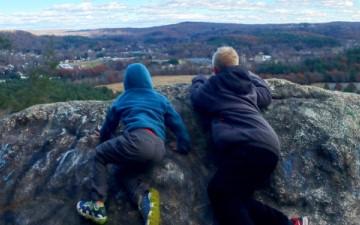 Two people lying on a large rock outcropping, looking out over a scenic valley view.